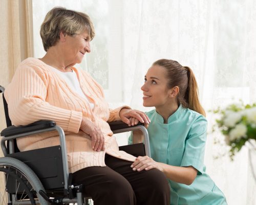 Elderly woman on wheelchair in nursing home with her care assistant